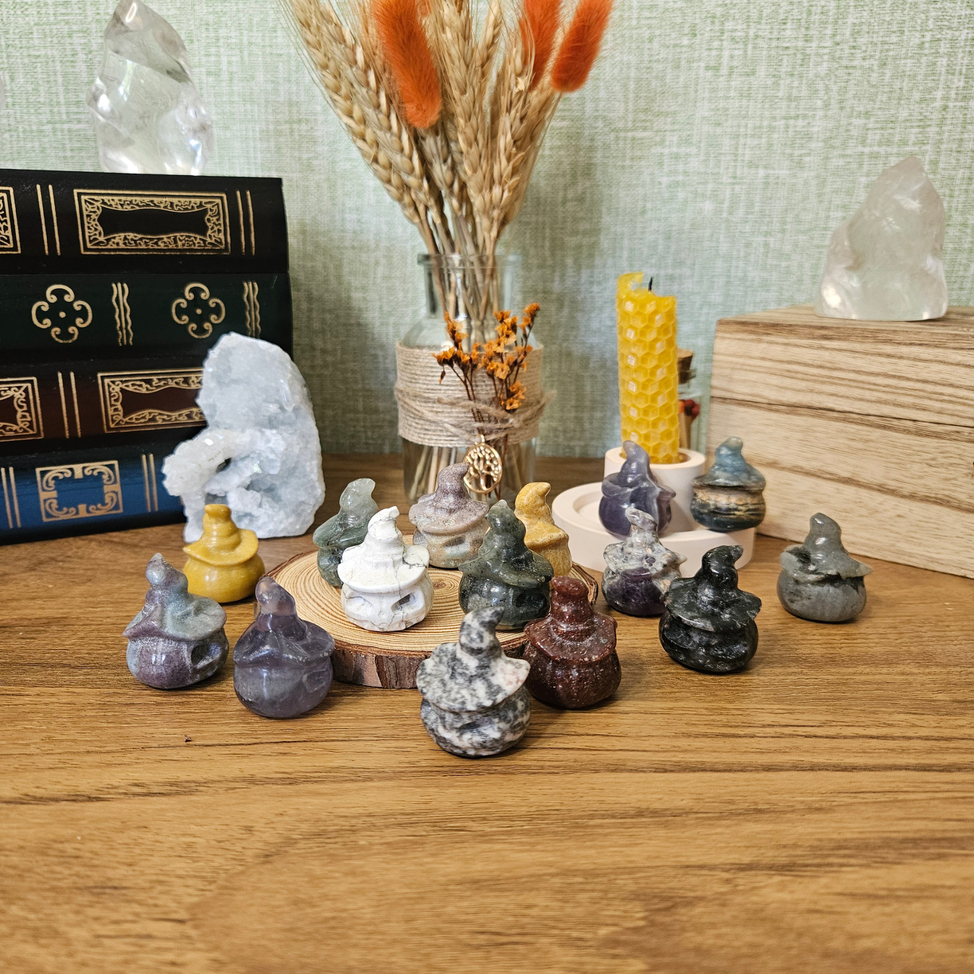 Collection of tiny crystal pumpkin witches in assorted stones displayed with crystals, dried flowers and a beeswax candle.