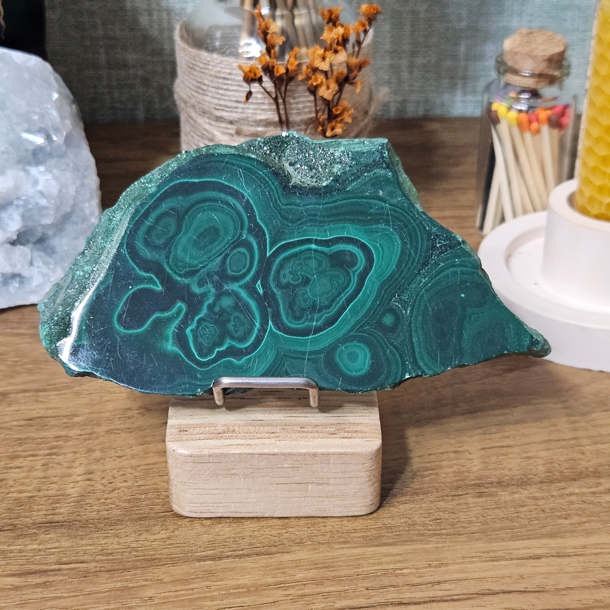 Natural Malachite slice with deep green banding, circular eye patterns and rough mineral edges.