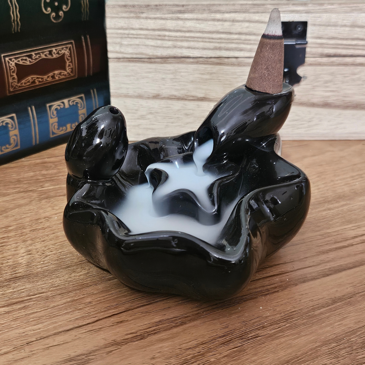 Black ceramic waterfall backflow incense burner with white incense smoke cascading into the lower pool.