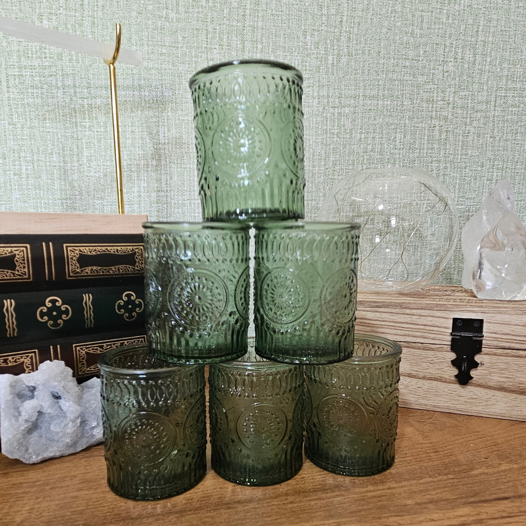 Green embossed glass tealight holder with decorative vintage-style pattern and lit candle creating a warm glow.