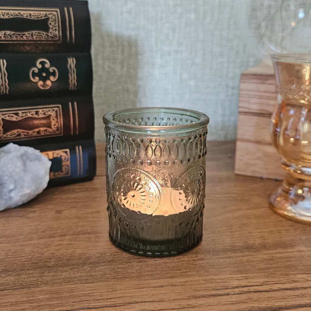 Green embossed glass tealight holder with decorative vintage-style pattern and lit candle creating a warm glow.