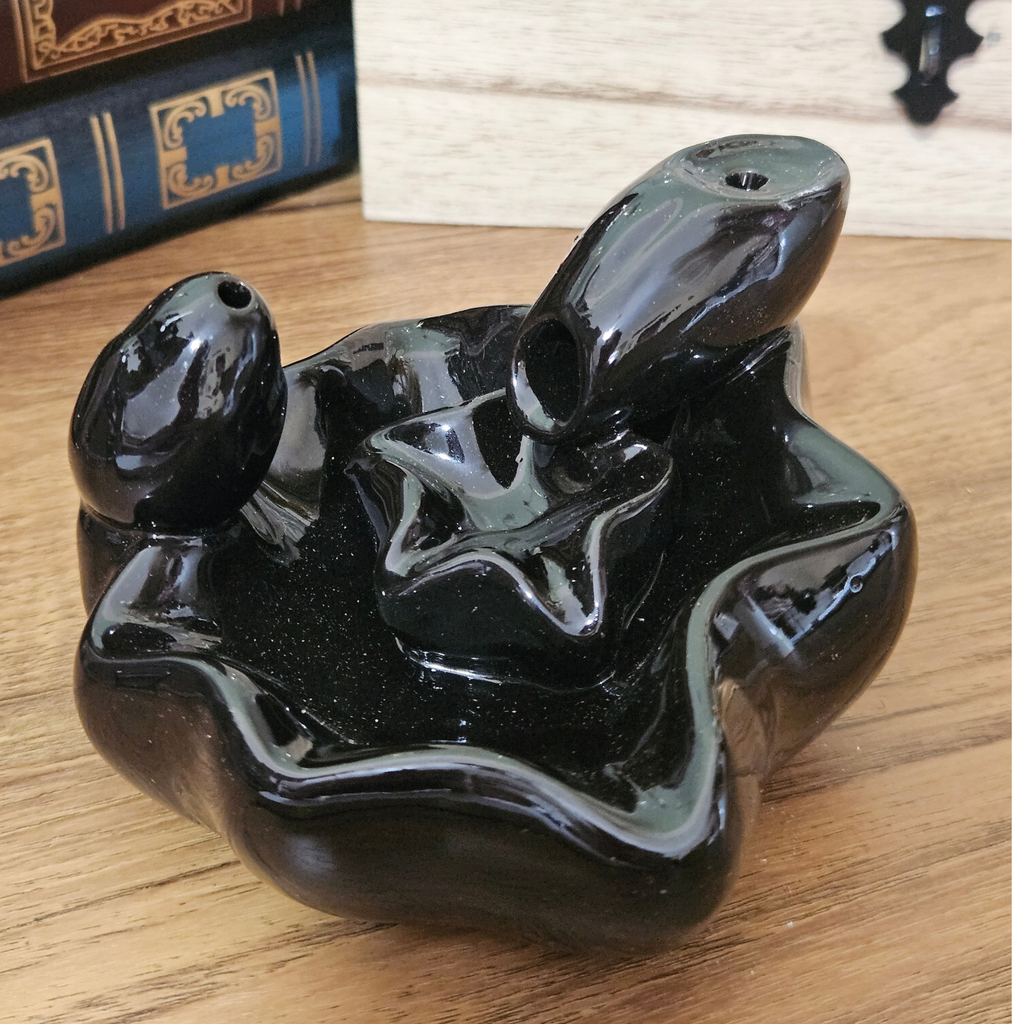 Black ceramic waterfall backflow incense burner with white incense smoke cascading into the lower pool.