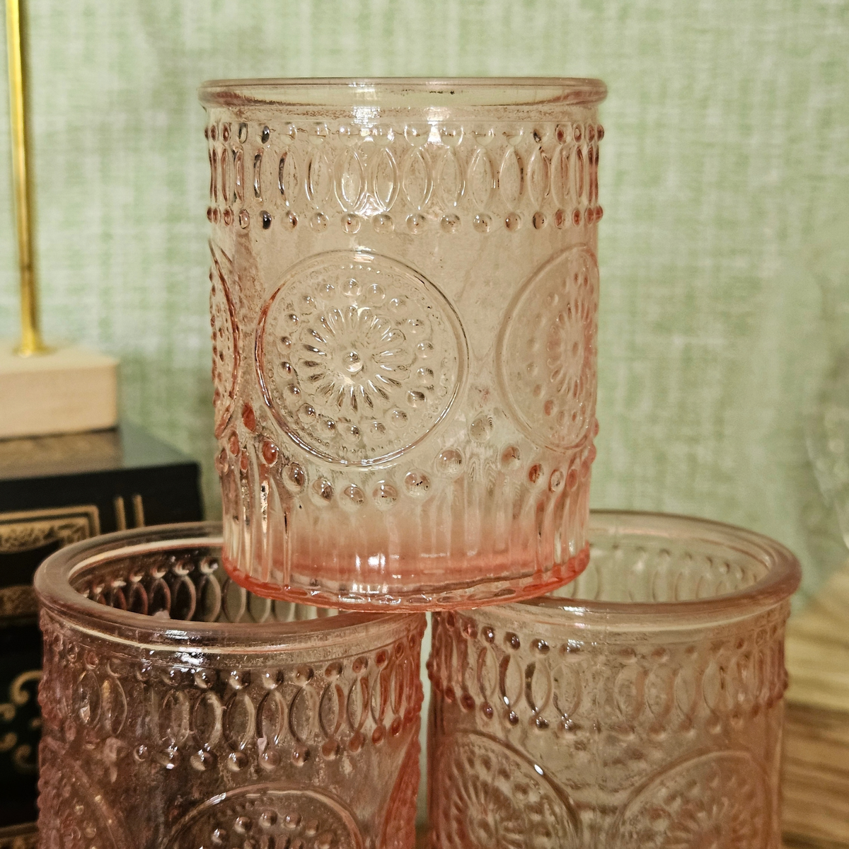 Pink embossed glass tealight holder with decorative vintage-style pattern and lit tealight candle.