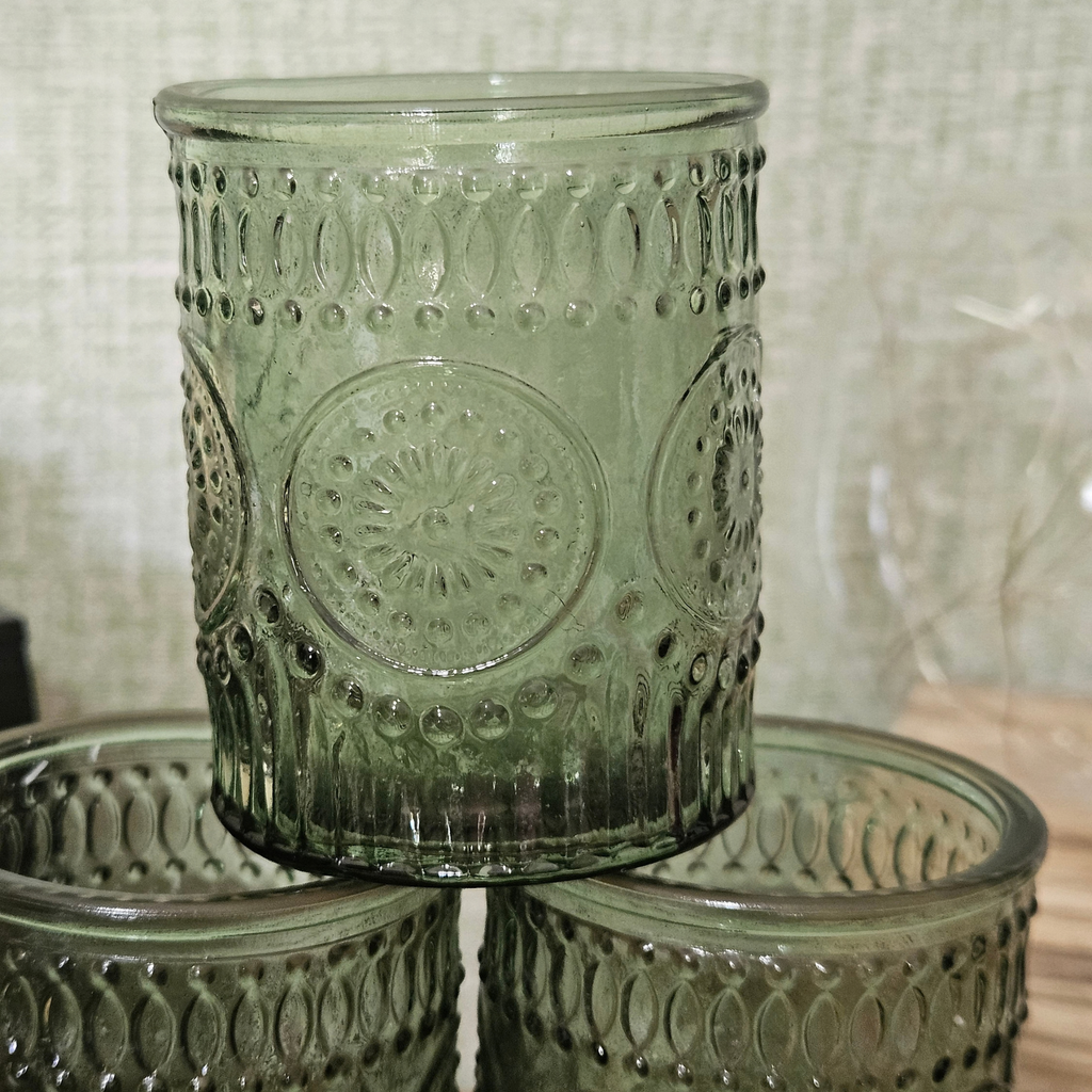 Green embossed glass tealight holder with decorative vintage-style pattern and lit candle creating a warm glow.