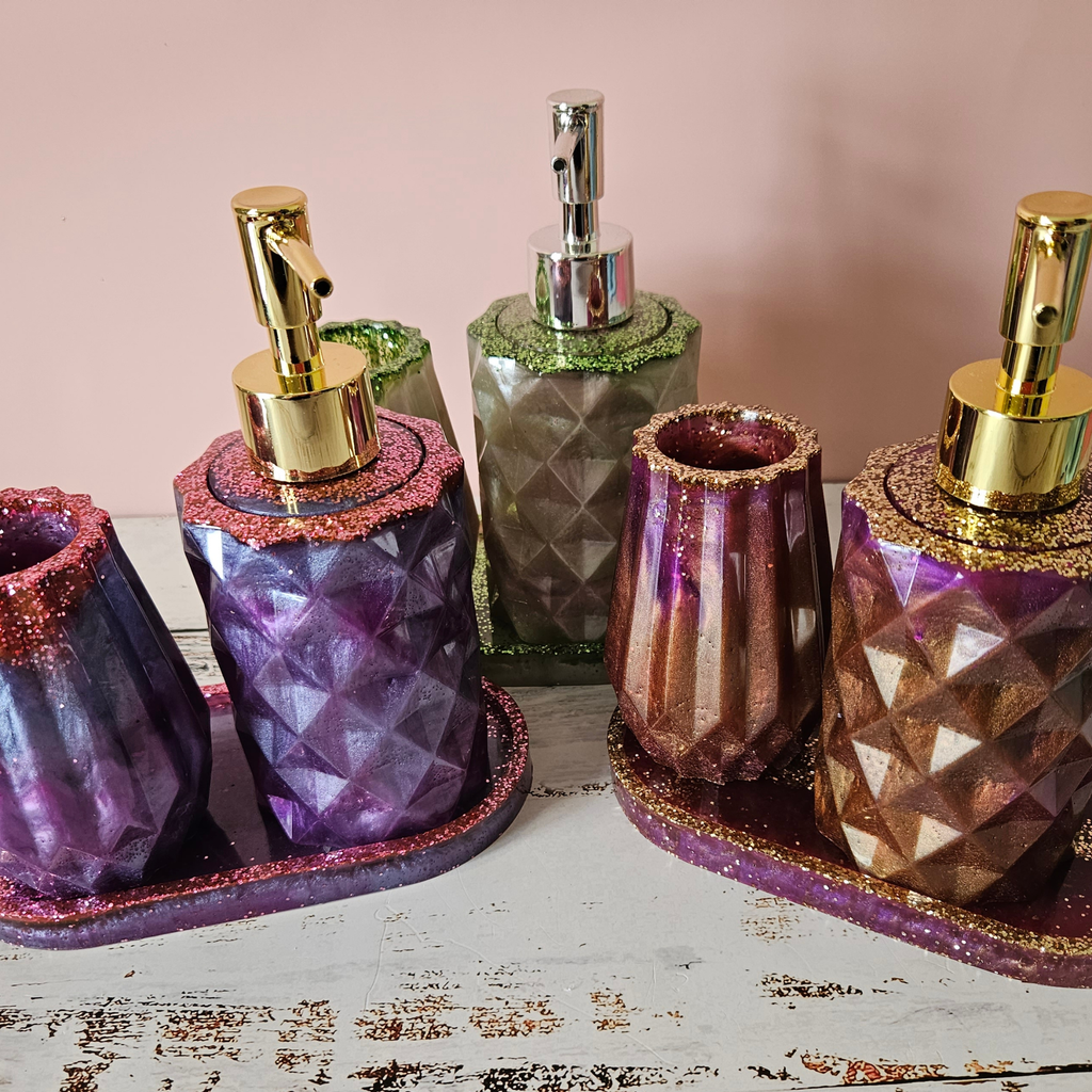 Three handmade resin bathroom sets in purple, gold and sage with soap dispensers, tumblers and matching trays