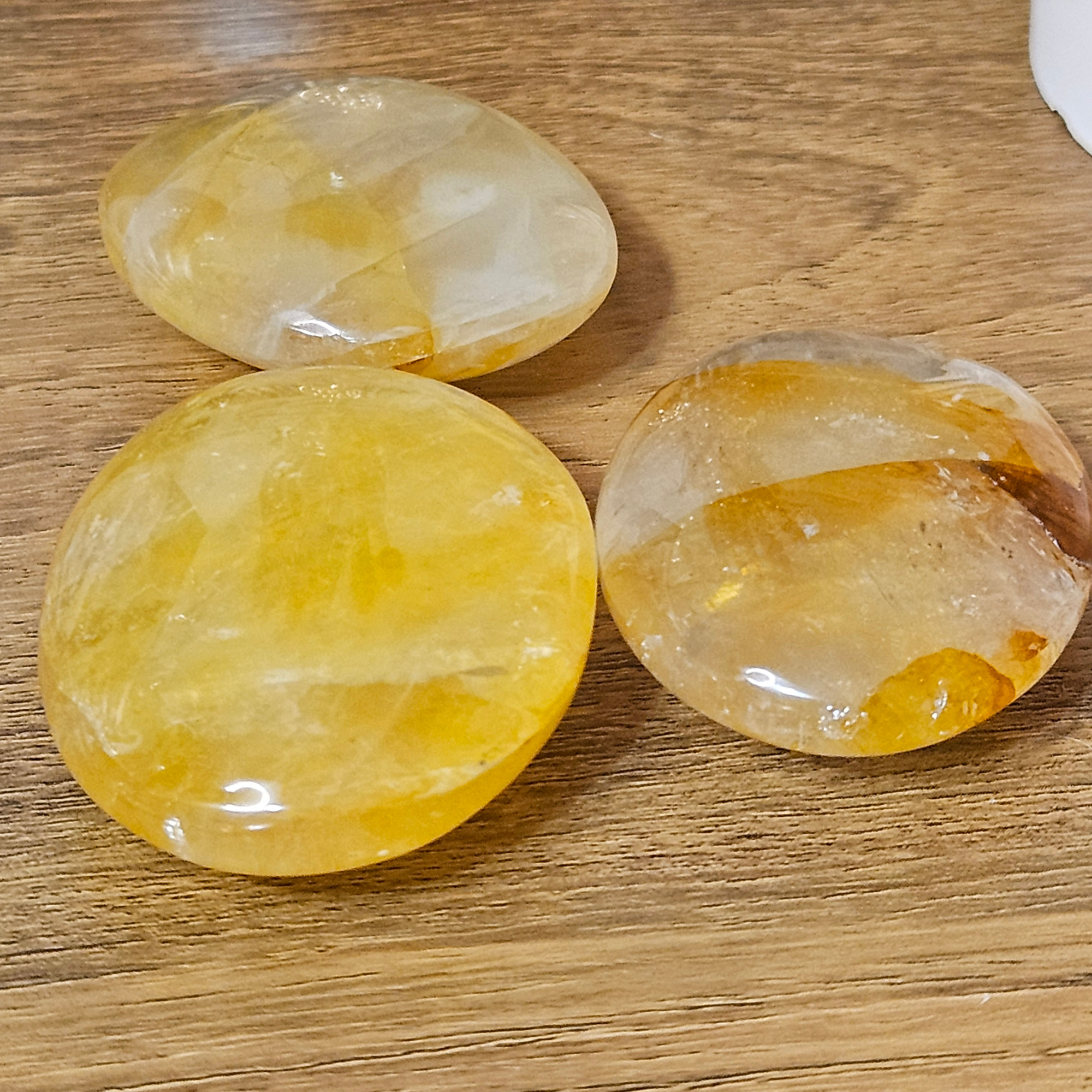 Three Golden Healer Quartz palm stones with natural yellow and golden iron inclusions.