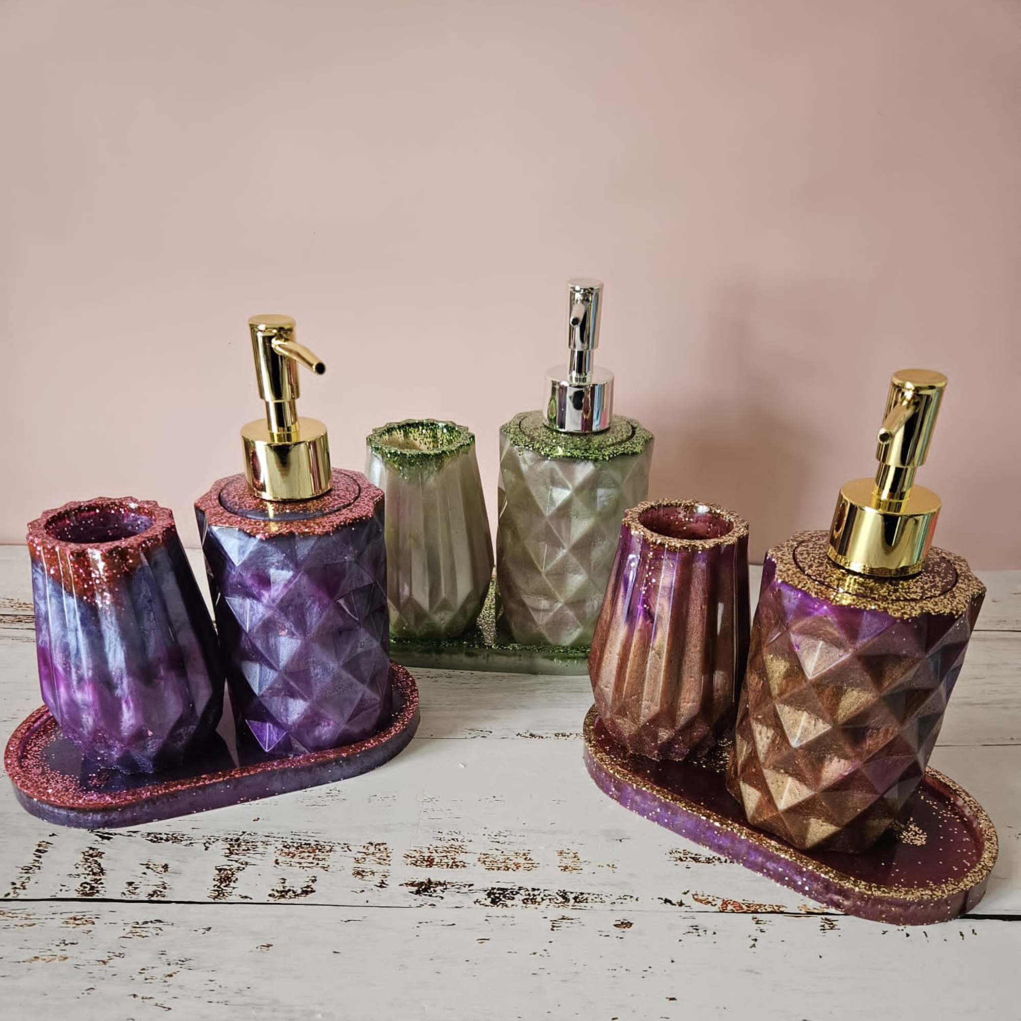 Three handmade resin bathroom sets in purple, gold and sage with soap dispensers, tumblers and matching trays