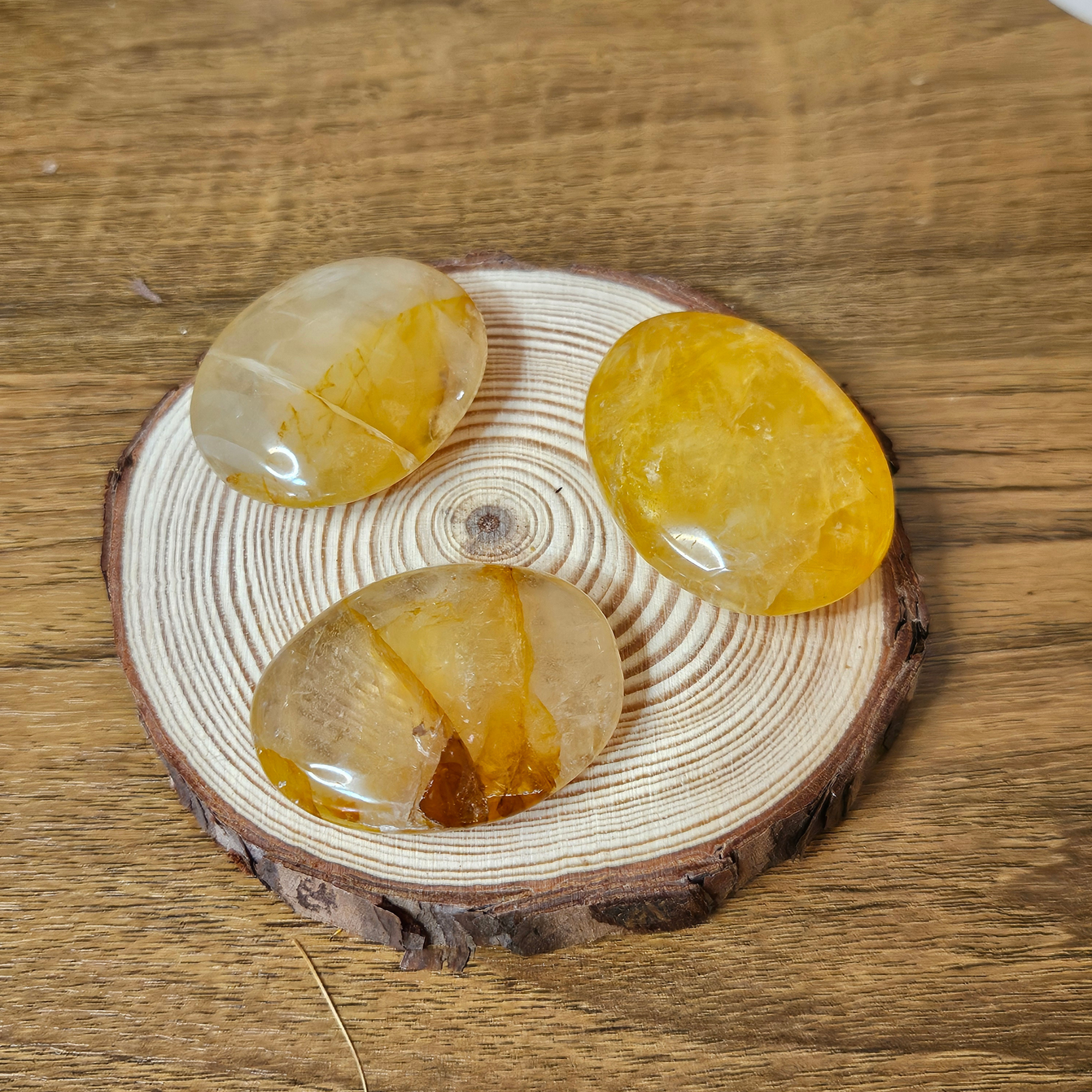 Three polished Golden Healer Quartz palm stones displayed on a natural wood slice.